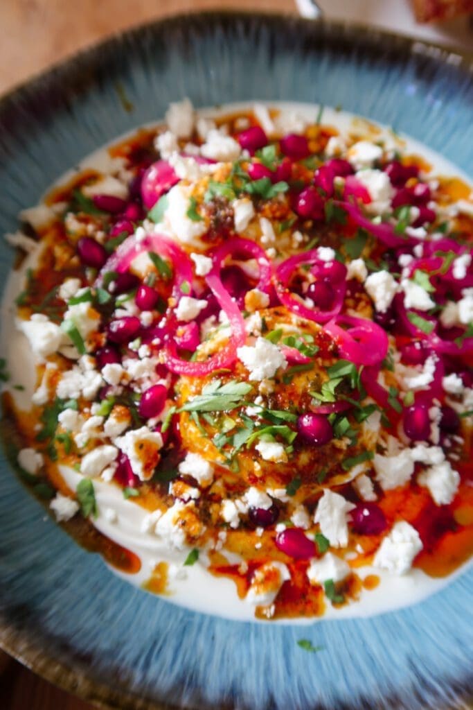 Bowl of Turkish eggs topped with spiced butter, pomegranate, feta and herbs