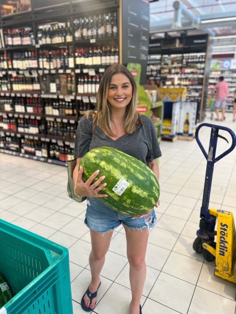 raveller holding a giant watermelon in a European supermarket — a playful reminder of how travel influences cooking and sparks creativity at home.