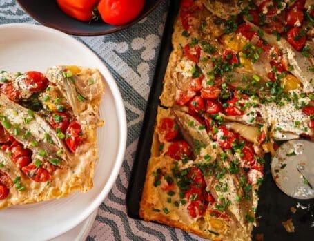 Overhead shot of a caramelised shallot and tomato tart glistening under golden puff pastry