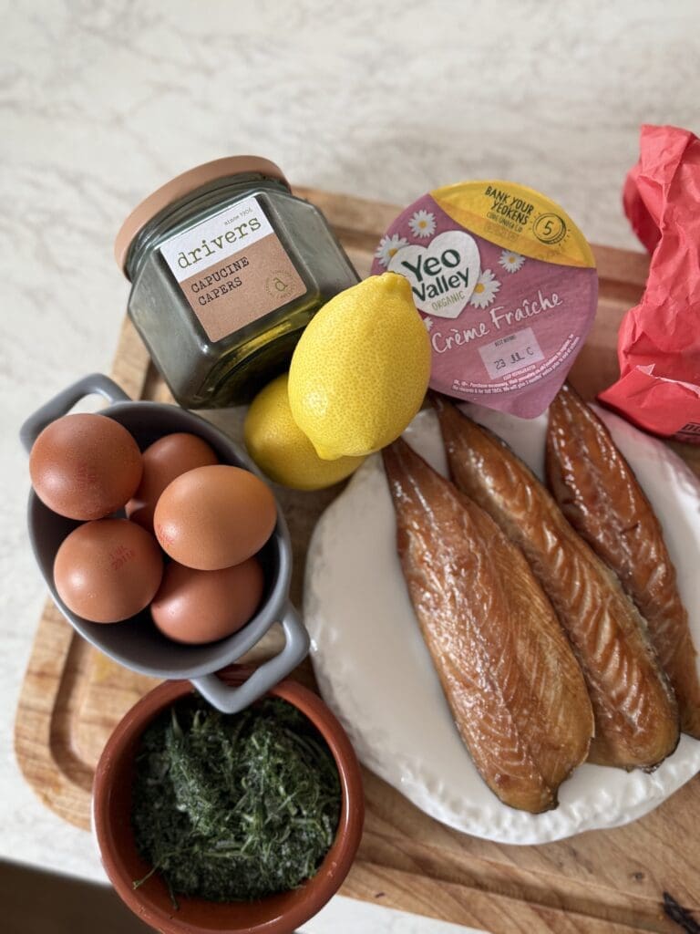 Flat lay of ingredients for Scandi-style breakfast, including eggs, smoked mackerel, tomatoes, and crème fraîche.