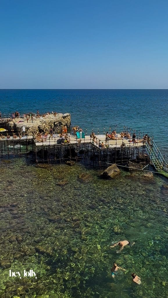 Wooden sunbathing platform with swimmers diving into clear turquoise waters in Ortigia