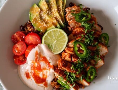 Chicken burrito bowl topped with sliced chicken, avocado, beans, sweetcorn, cheddar, and chilli cream drizzle.