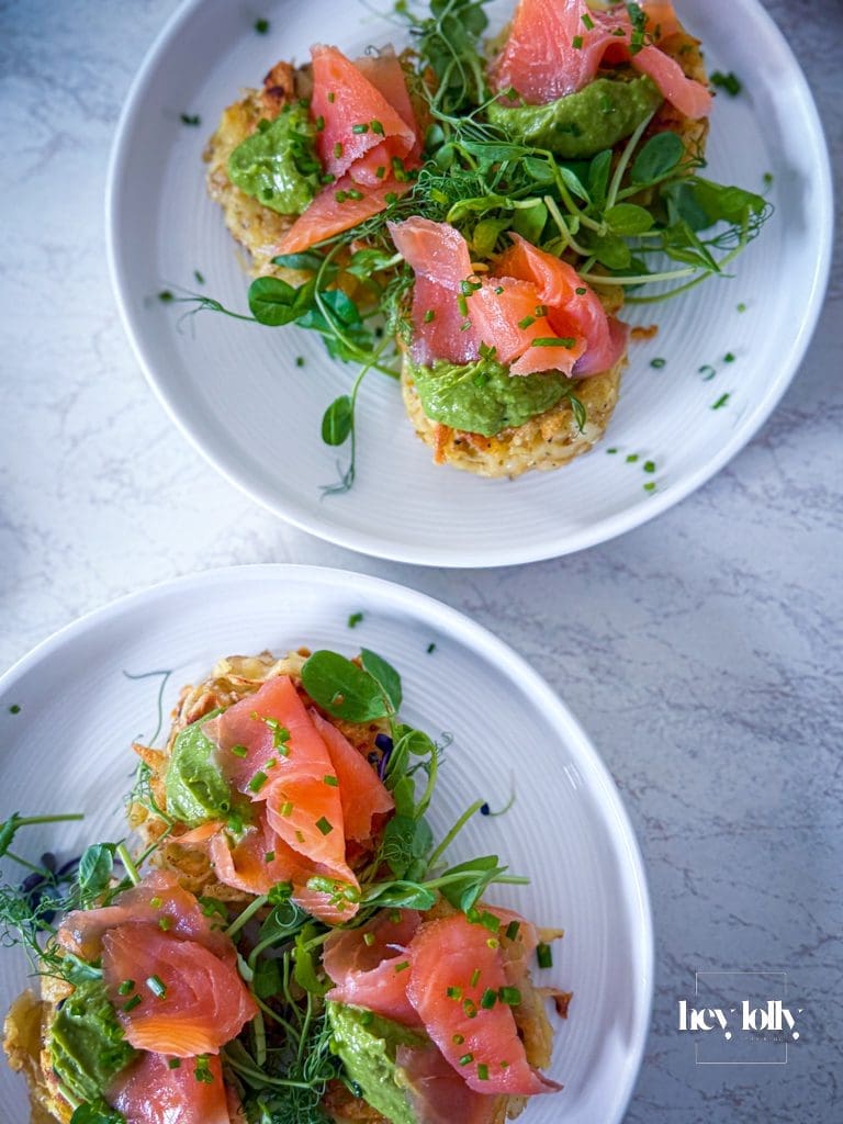 Potato cakes topped with avocado cream and smoked salmon, finished with dill and lemon wedges.