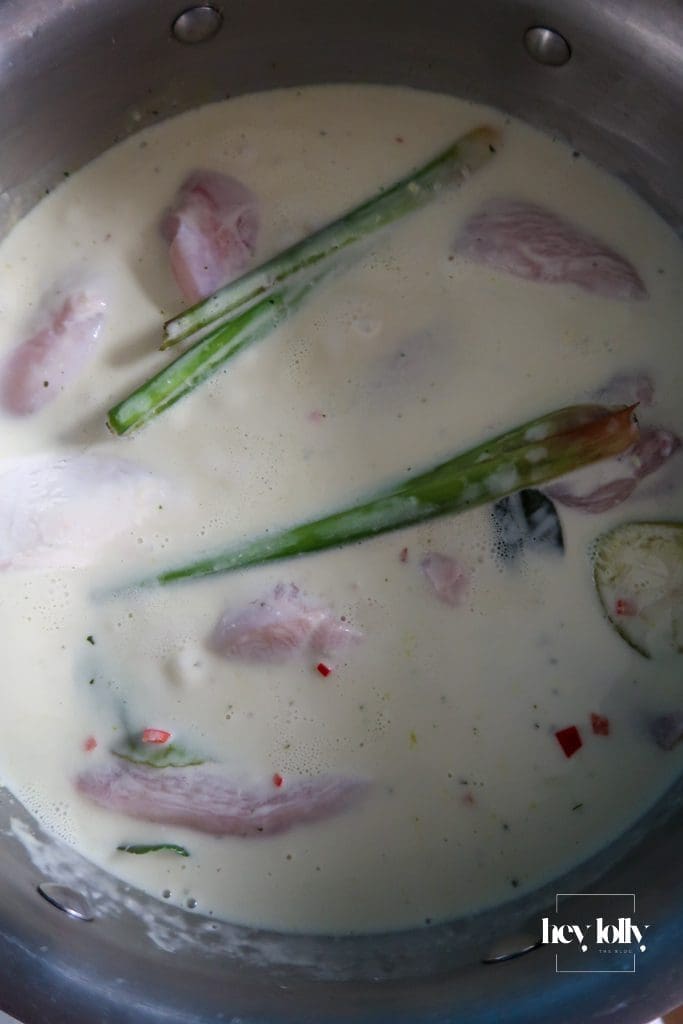Coconut milk poaching liquid simmering with lemongrass, ginger, garlic, and kaffir lime leaves for Thai poached chicken salad.