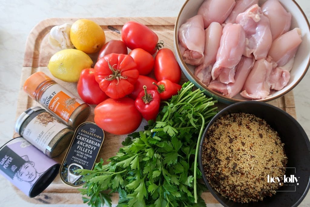 Flat lay of ingredients for Za’atar Chicken Thighs recipe including chicken thighs, za’atar, cumin, tomatoes, and anchovies
