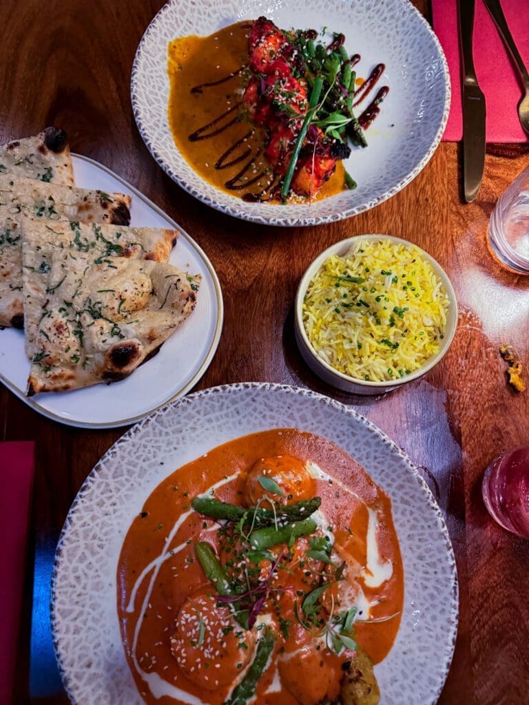Overhead shot of mains at Passan’s Nottingham — Tandoori Monkfish, Malai Chicken, Garlic Naan, and Pilau Rice served on a dark wooden table.