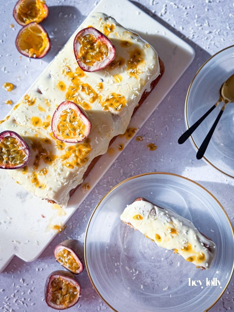 Finished passion fruit yoghurt loaf with cream cheese frosting and glossy passion fruit drizzle, golden and vibrant on white plate.