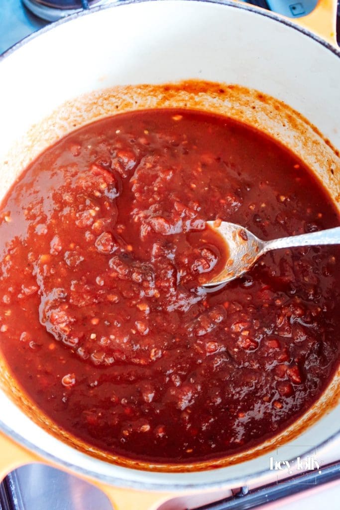 Garlic and chipotle paste bubbling in tomato sauce on the hob — rich red colour and steam rising.