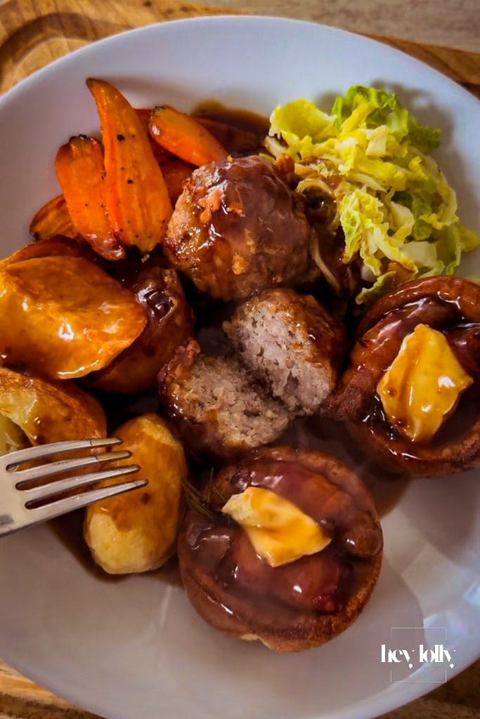Pork and stuffing roast bombs over roast potatoes and greens with glossy gravy poured.