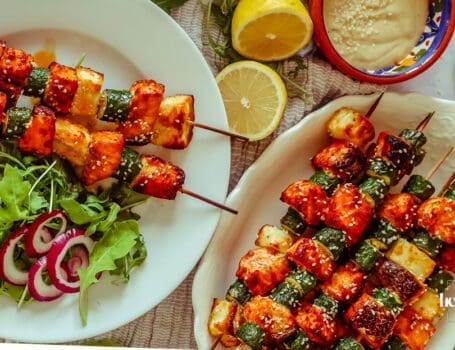 Salmon, Courgette & Halloumi Skewers with Lemon Tahini Dressing, topped with herbs and lemon wedges.