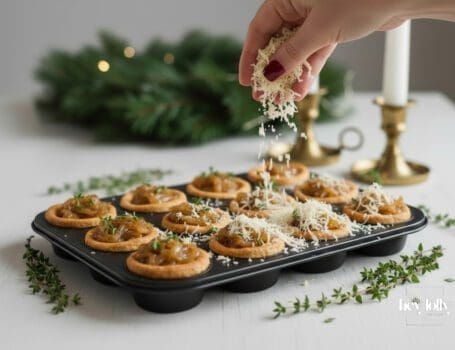Sprinkling grated Gruyère over onion-filled tartlet cases to make caramelised onion and Gruyère mini tartlets.