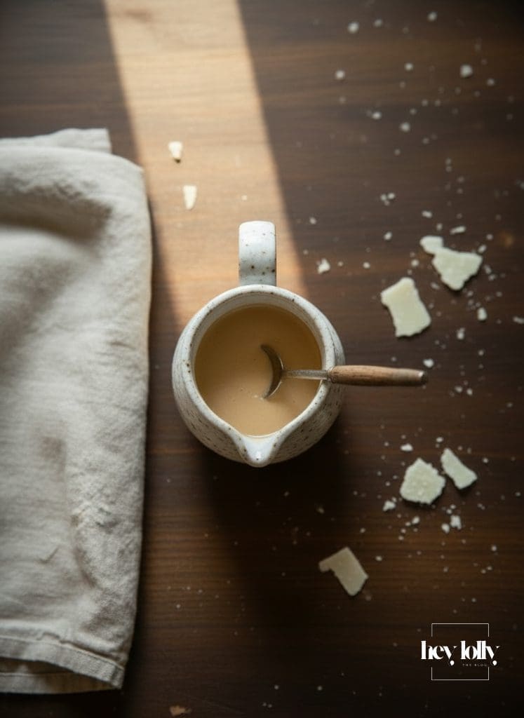 Creamy Caesar dressing in a ceramic jug with black pepper flecks on a wooden table