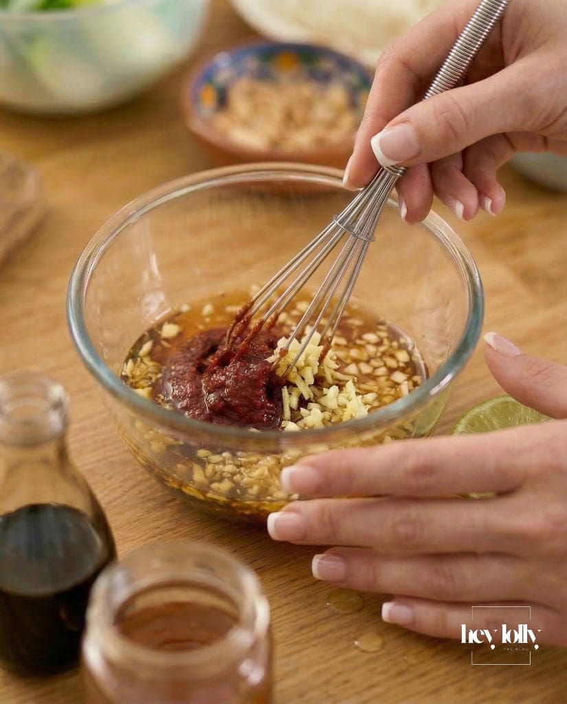 Yuzu gochujang sauce being whisked in a bowl with soy sauce, sesame oil, garlic and ginger.