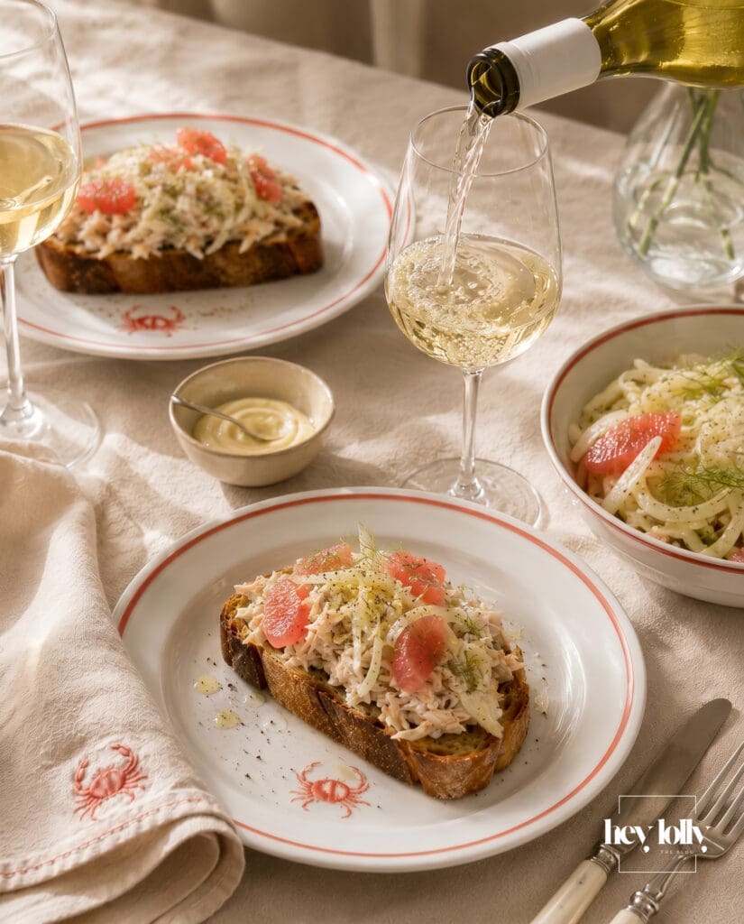 Several plates of crab toast with fennel and grapefruit salad styled on an ivory linen hosting table with coastal editorial styling.