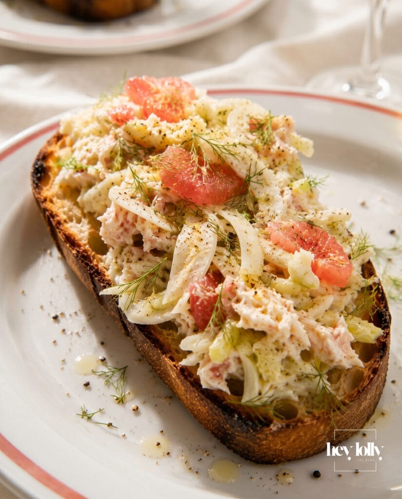 Crab toast with fennel and grapefruit salad on coral-rimmed crab plates with white wine and ivory linen table styling.