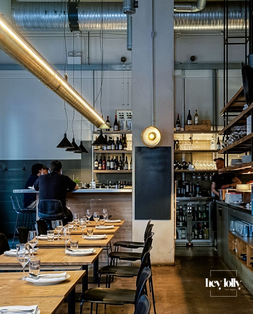 Minimalist dining room interior inside Erst Manchester with pale wood tables, black chairs and open kitchen shelving – Erst Manchester review