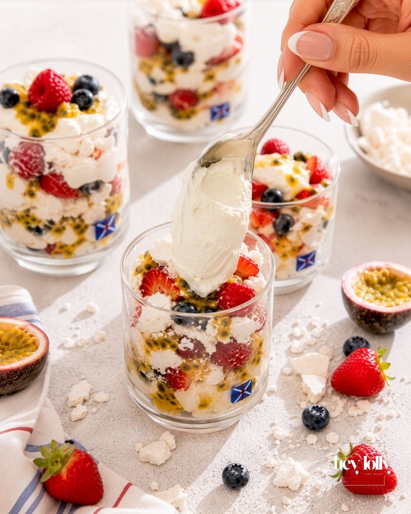 Spoon lifting cream, berries, meringue and passion fruit from a summer pavlova cup.