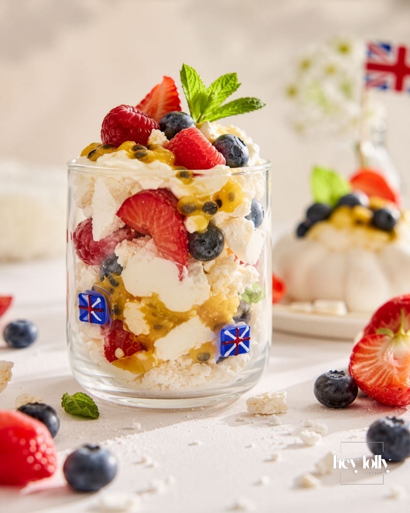 Summer pavlova cup layered with whipped cream, crushed meringue, berries and passion fruit in a clear glass tumbler.