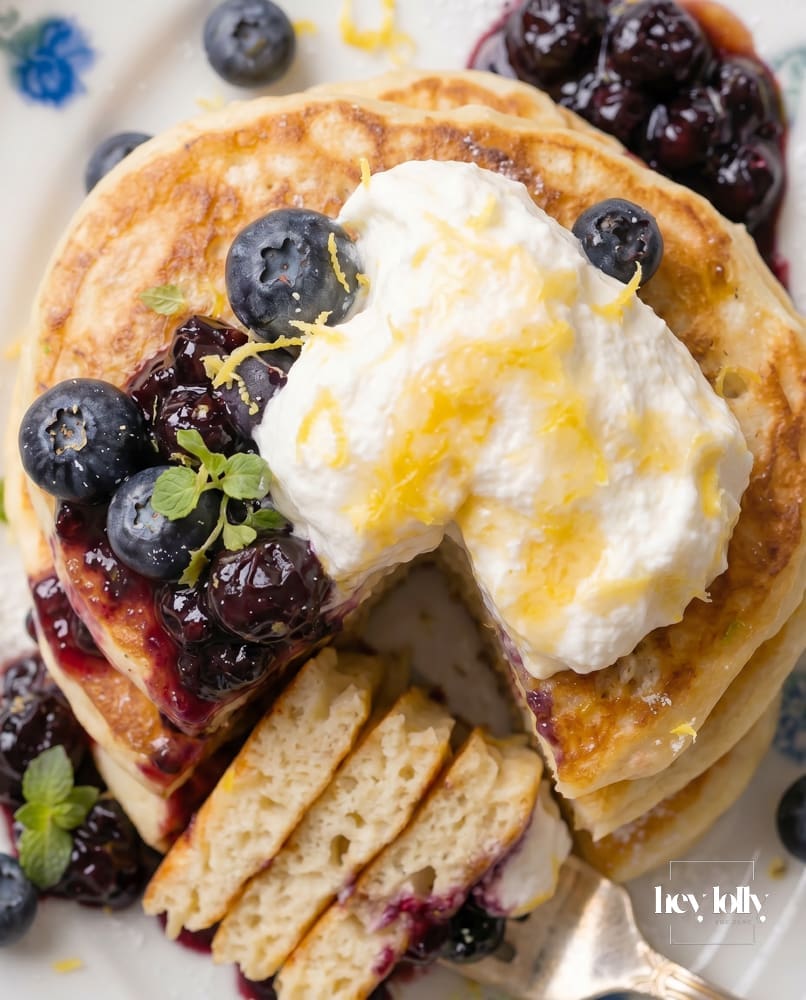Fork lifting a soft bite of lemon ricotta pancakes, showing the fluffy inside with blueberry compote and cream.